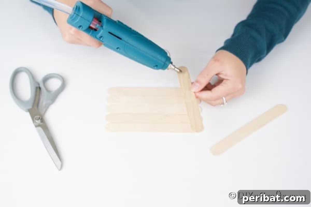 Whimsical Wooden Gingerbread House Charm 7 Step-by-step image showing how to glue craft sticks together for the roof of a gingerbread house ornament
