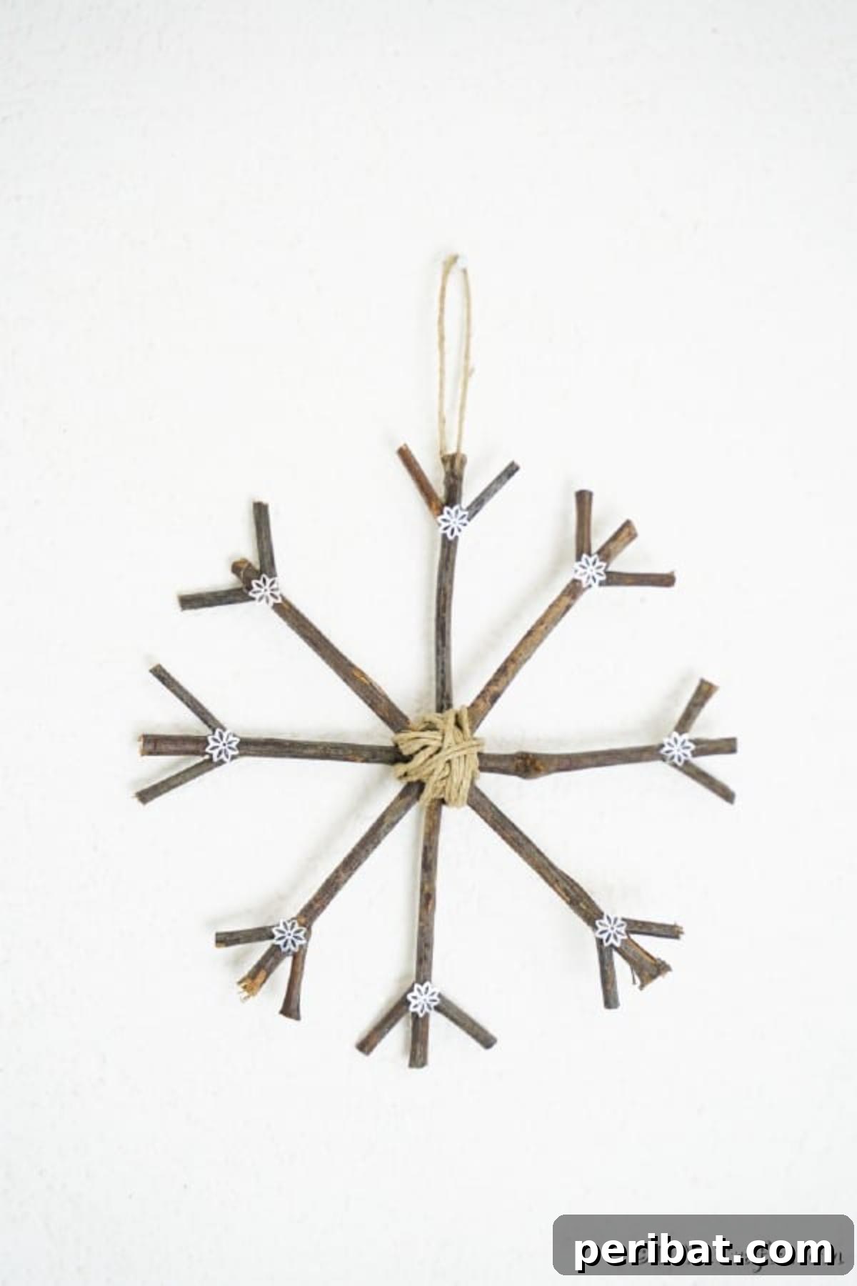 DIY Rustic Twig and Branch Christmas Ornaments 18 A beautifully crafted snowflake rustic Christmas ornament hanging delicately on a white wall, showcasing its detailed design.