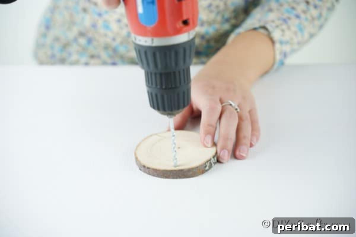 Rustic Wood Slice Chalkboard Charm 7 Close-up of a hand drilling a precise hole into the top edge of a round wooden slice, preparing it for a hanging ornament, with wood shavings visible around the drill bit.
