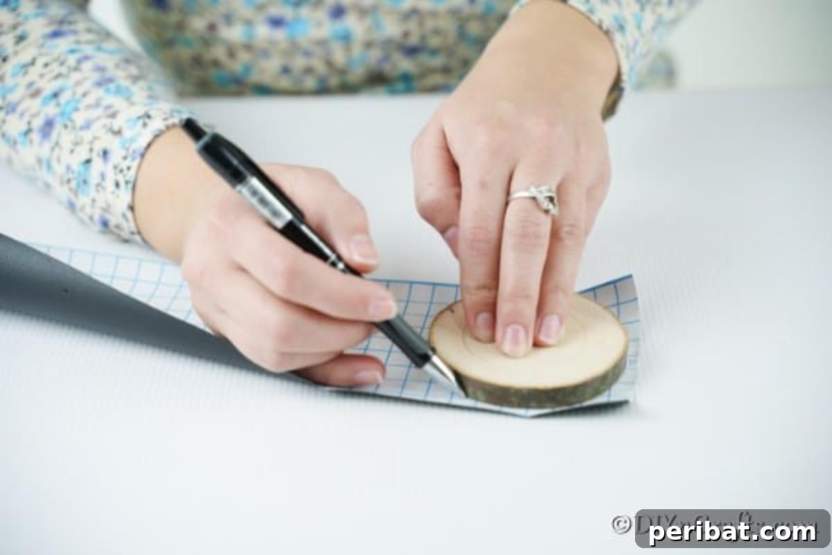 Rustic Wood Slice Chalkboard Charm 8 A hand meticulously tracing the outline of a wooden slice onto a sheet of black chalkboard paper with a pencil, preparing the material for a DIY chalkboard ornament project.