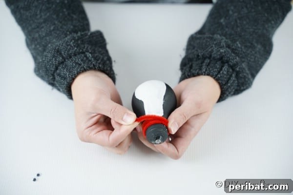 Adding the red pipe cleaner to the penguin lightbulb ornament