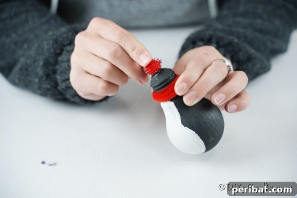 Gluing a red pom pom on top of a light bulb penguin decoration