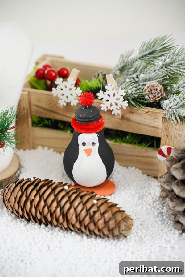 A penguin lightbulb ornament in front of a wooden box filled with holiday decorations