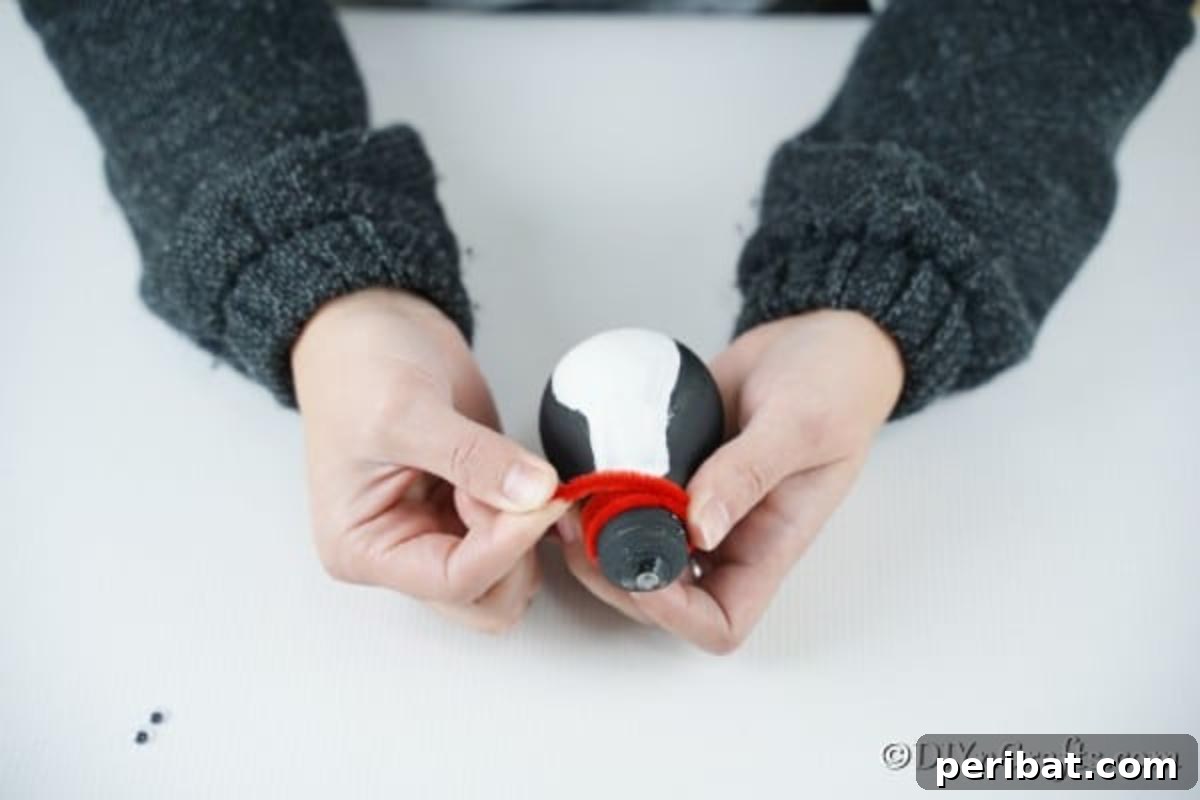 Adding the red pipe cleaner to the penguin lightbulb ornament