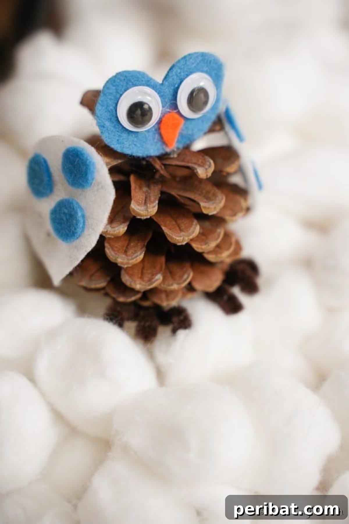 Whimsical Winter Pinecone Owl Decorations 3 A pinecone owl decoration sitting on a bed of cotton balls, symbolizing snow