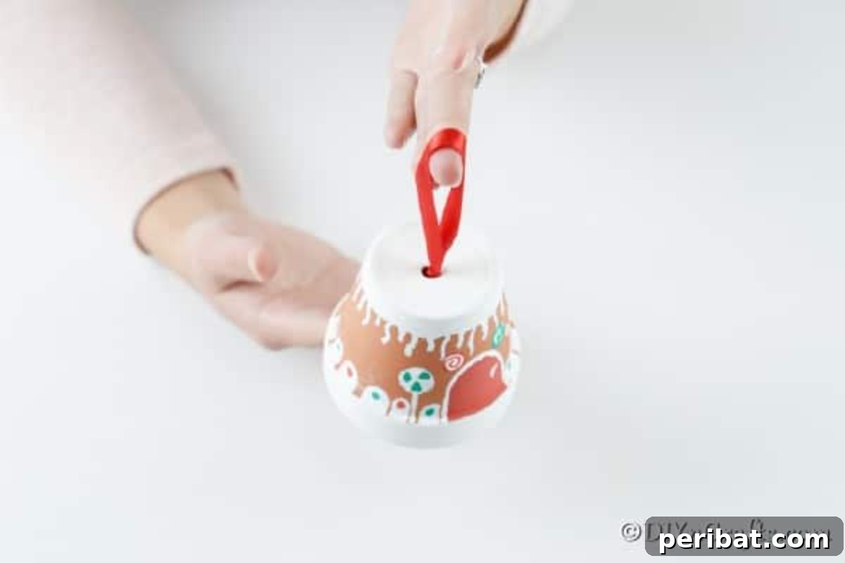 Threading a red satin ribbon through the drainage hole at the top of the flower pot to create a hanger for the gingerbread house.