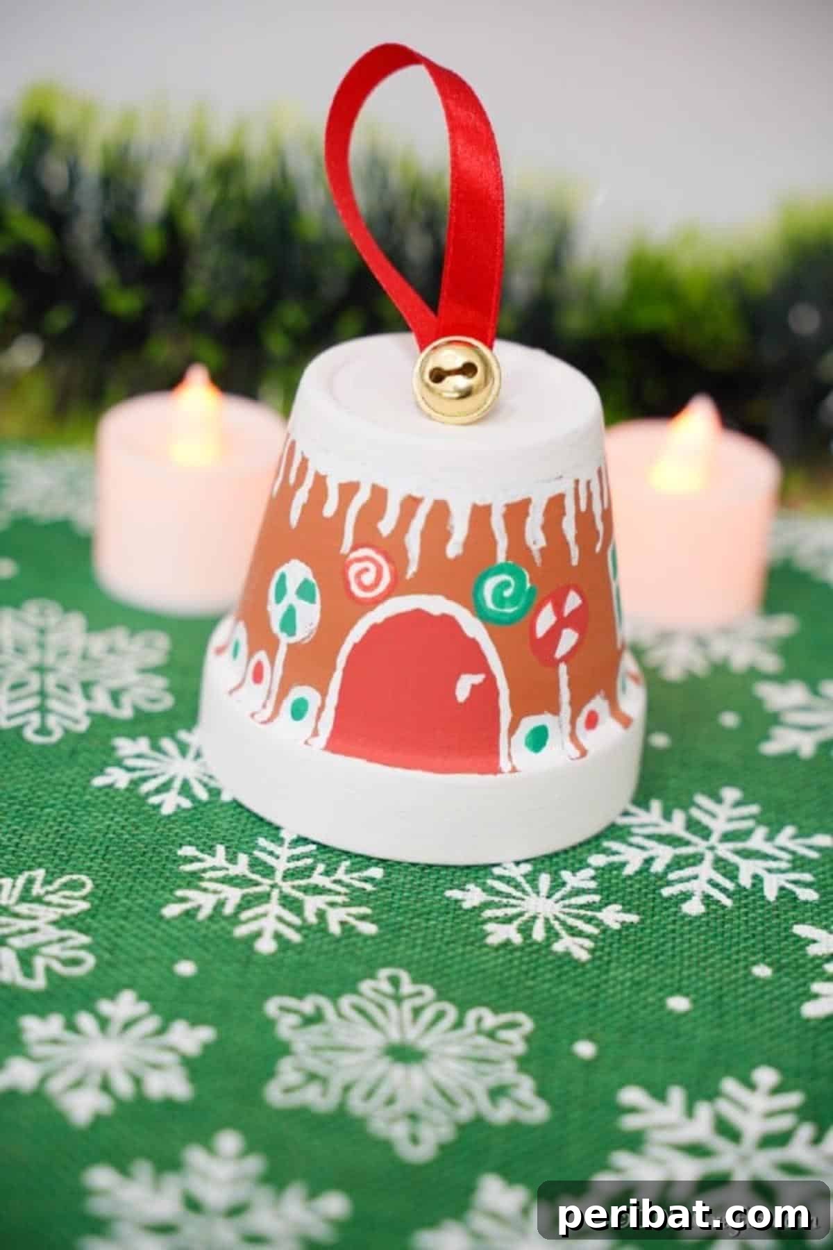 A detailed close-up of a gingerbread house made from a flower pot, featuring intricate white icicle designs and colorful candy-like decorations on a festive snowflake-patterned surface.