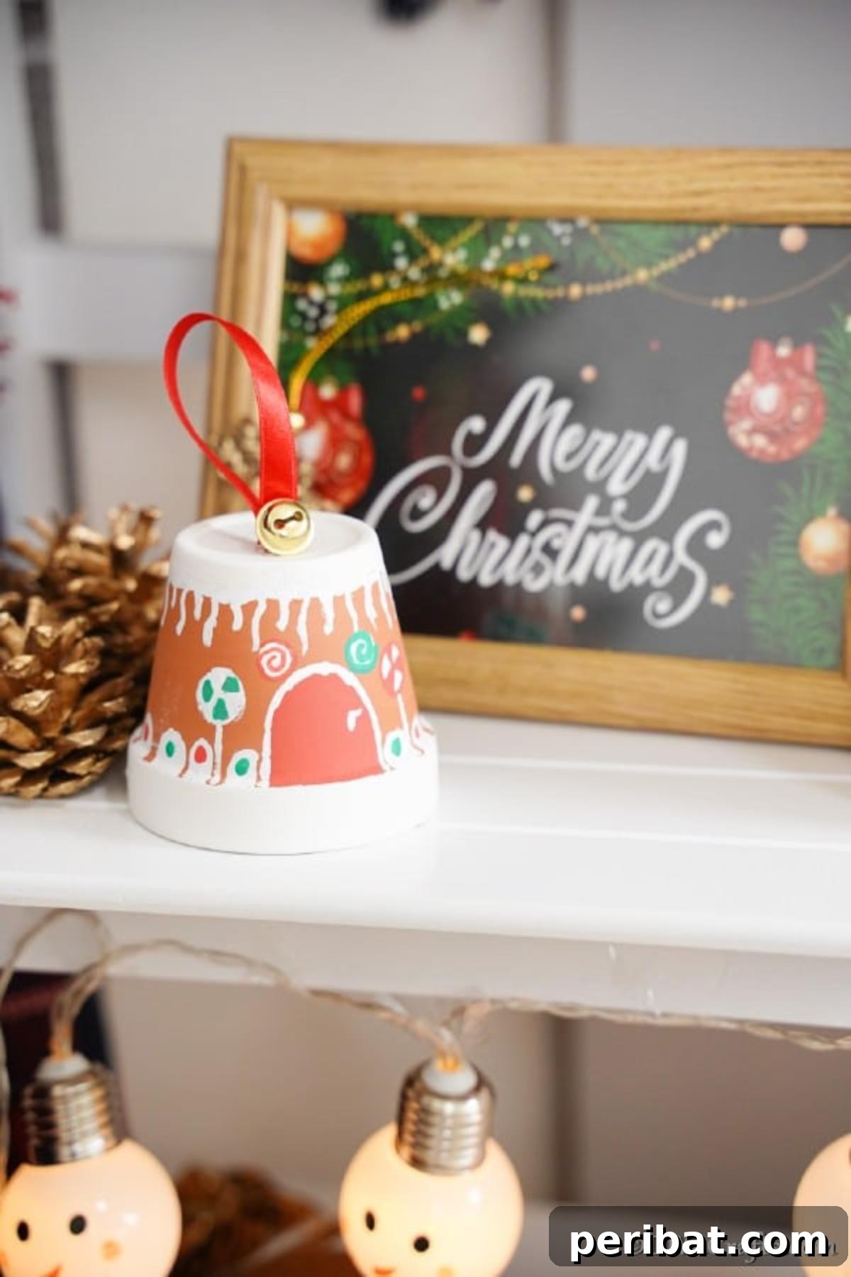 A festive flower pot gingerbread house sits on a white shelf, framed by a whimsical 'Merry Christmas' sign and other holiday decorations.