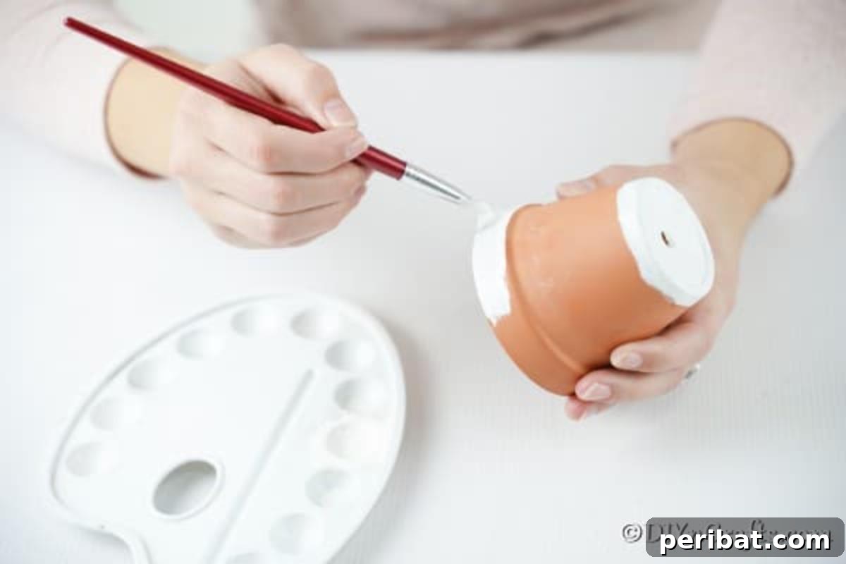 Applying the first coat of white paint to the base of the inverted clay pot, allowing drips for an icicle effect.