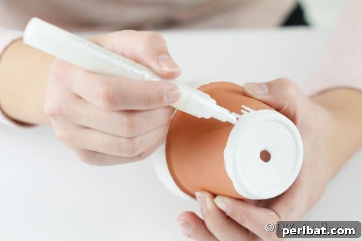 Using a white paint marker to draw detailed icicles along the top rim of the gingerbread house flower pot.