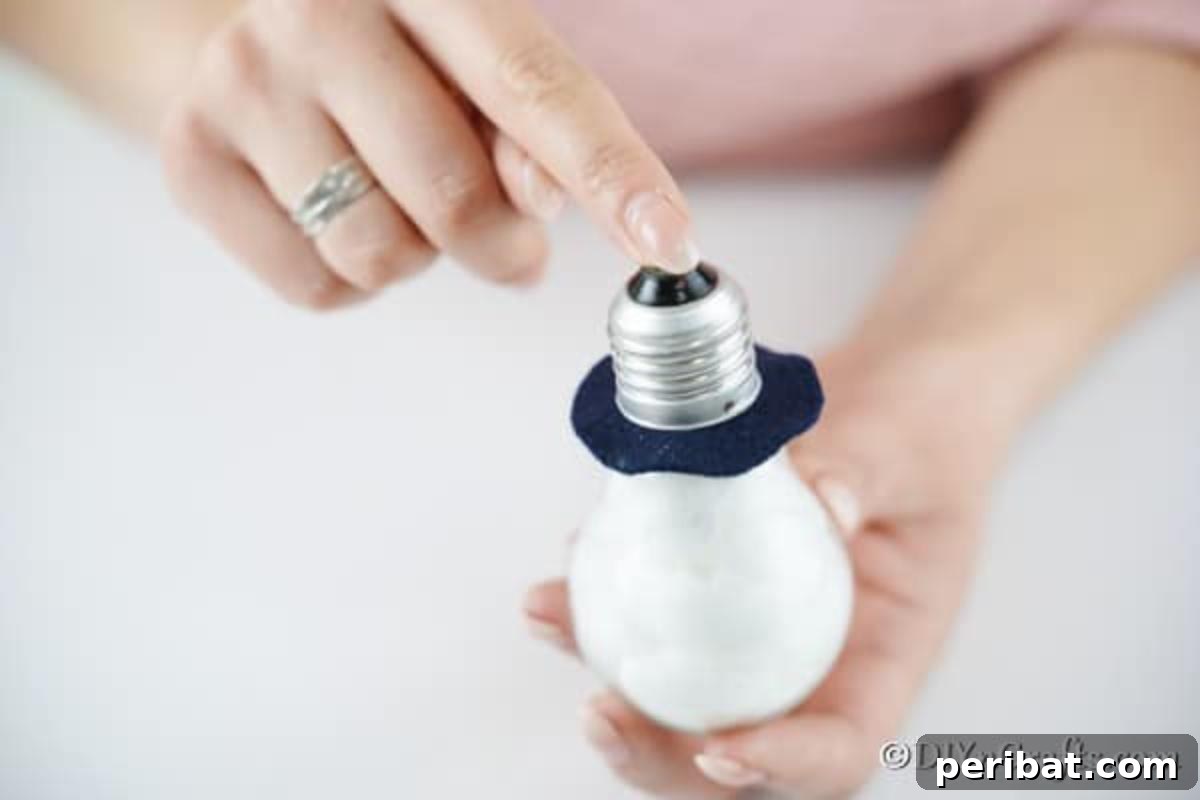 Close-up of the light bulb snowman ornament as the top piece is being carefully glued back into place, securing the hat