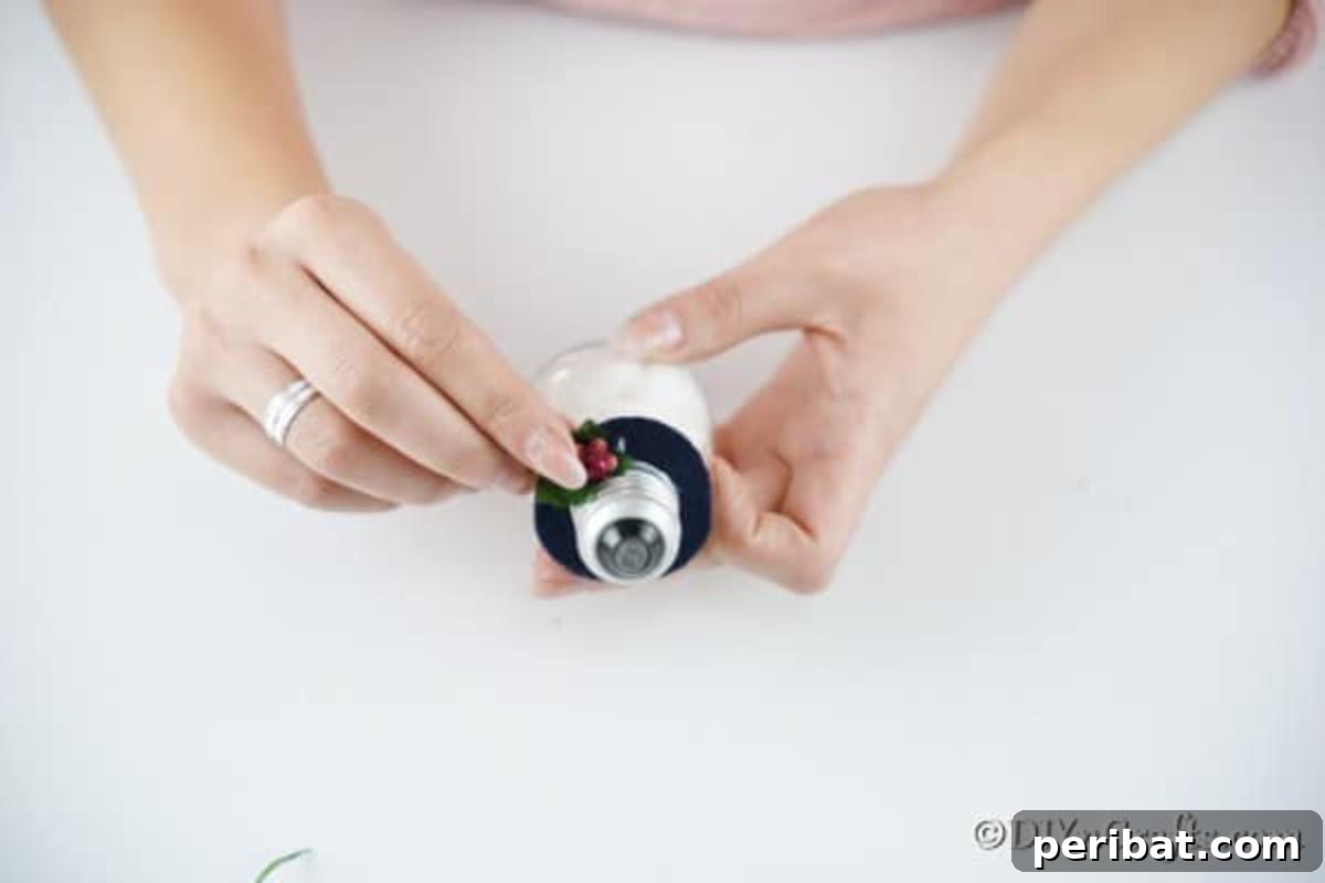 The process of adding small, decorative berries to the black felt hat of the snowman ornament, enhancing its festive appeal