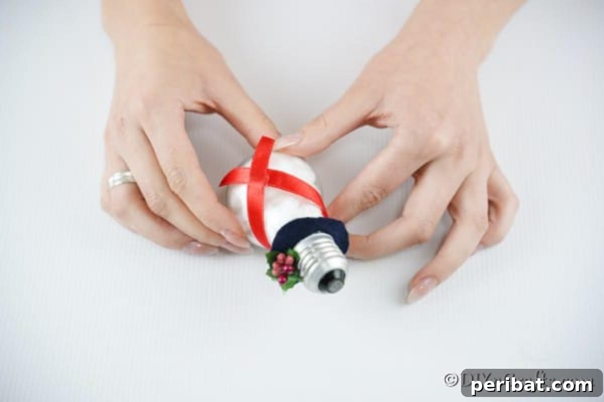 The step where a piece of festive ribbon is being carefully glued onto the light bulb snowman to form its scarf