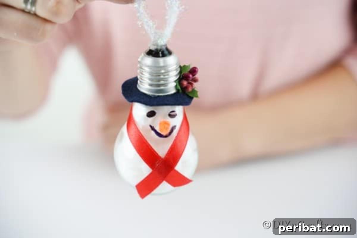 The final step of attaching a loop of twine to the top back of the light bulb snowman ornament for hanging