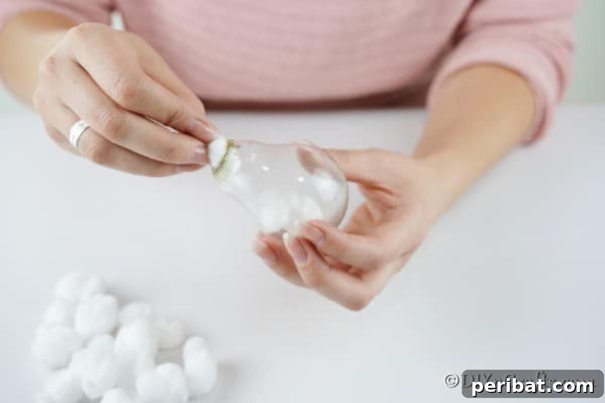 Process of carefully stuffing the hollowed-out light bulb with soft cotton balls, preparing it to become a snowman