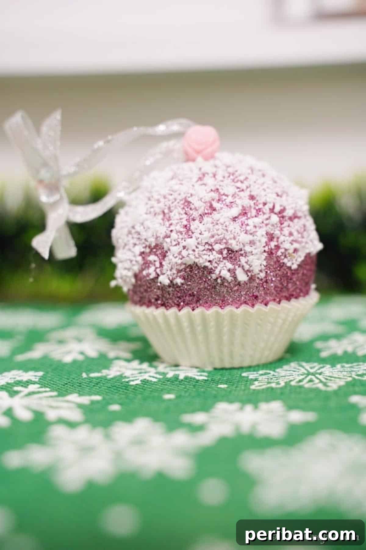 Sparkling DIY Cupcake Christmas Ornaments 5 A sparkling muffin ornament resting on a green and white snowflake patterned surface, highlighting its festive details