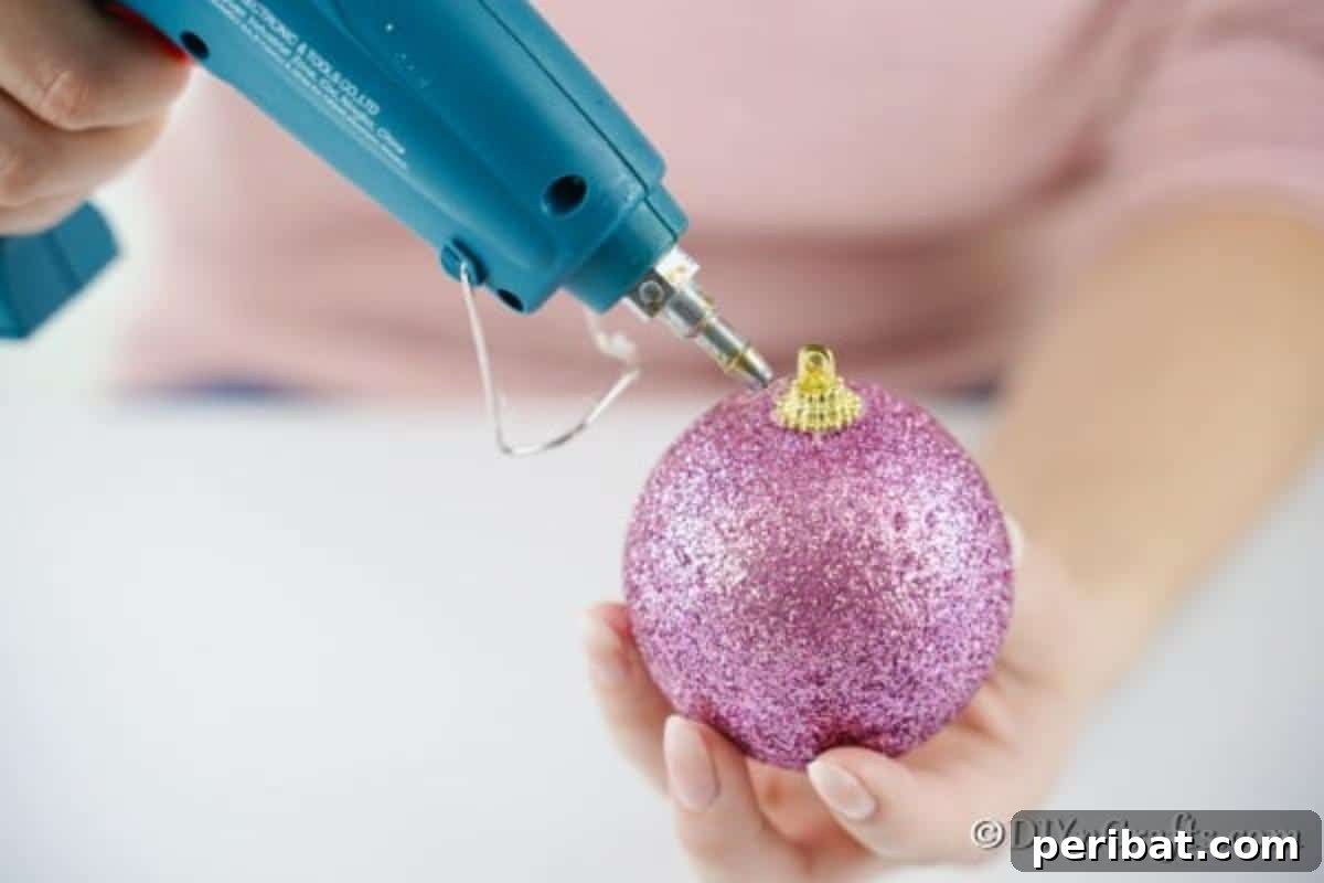Sparkling DIY Cupcake Christmas Ornaments 7 Applying hot glue in a circular motion to the top of a Christmas ball, mimicking dripping icing