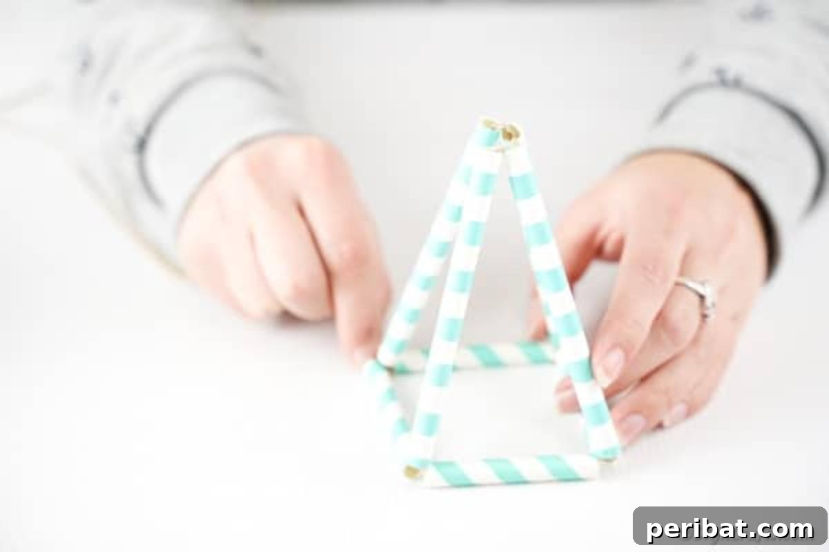 Hands gently pulling the paper straws together, shaping them into a delicate 3D triangular planter form, secured by taut twine.
