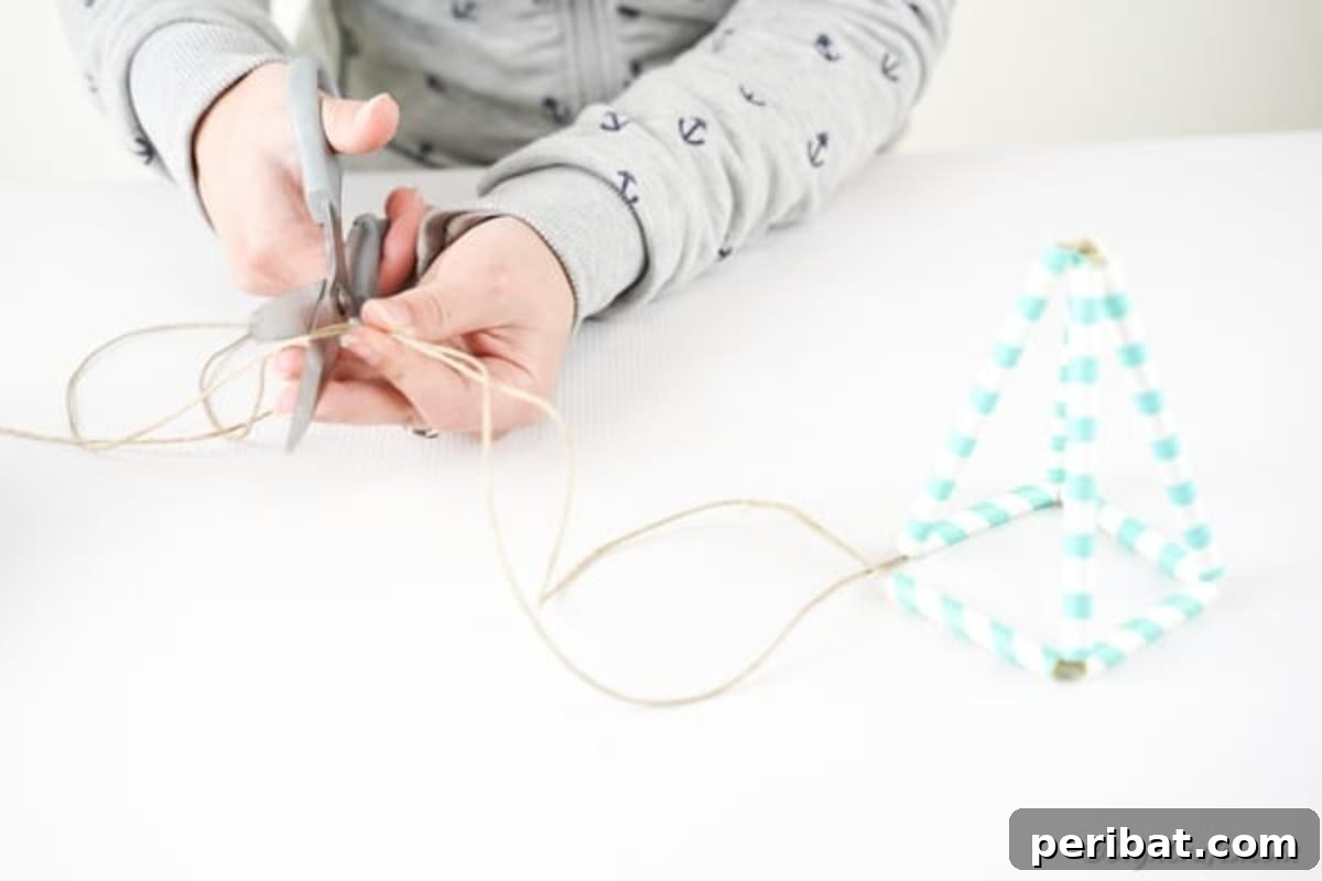 A close-up shot of twine being cut, leaving several inches loose at the end, demonstrating the preparation for hanging a succulent planter.