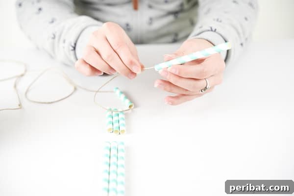 Twine being threaded through the first three paper straws (short, long, long) to begin forming the structure.