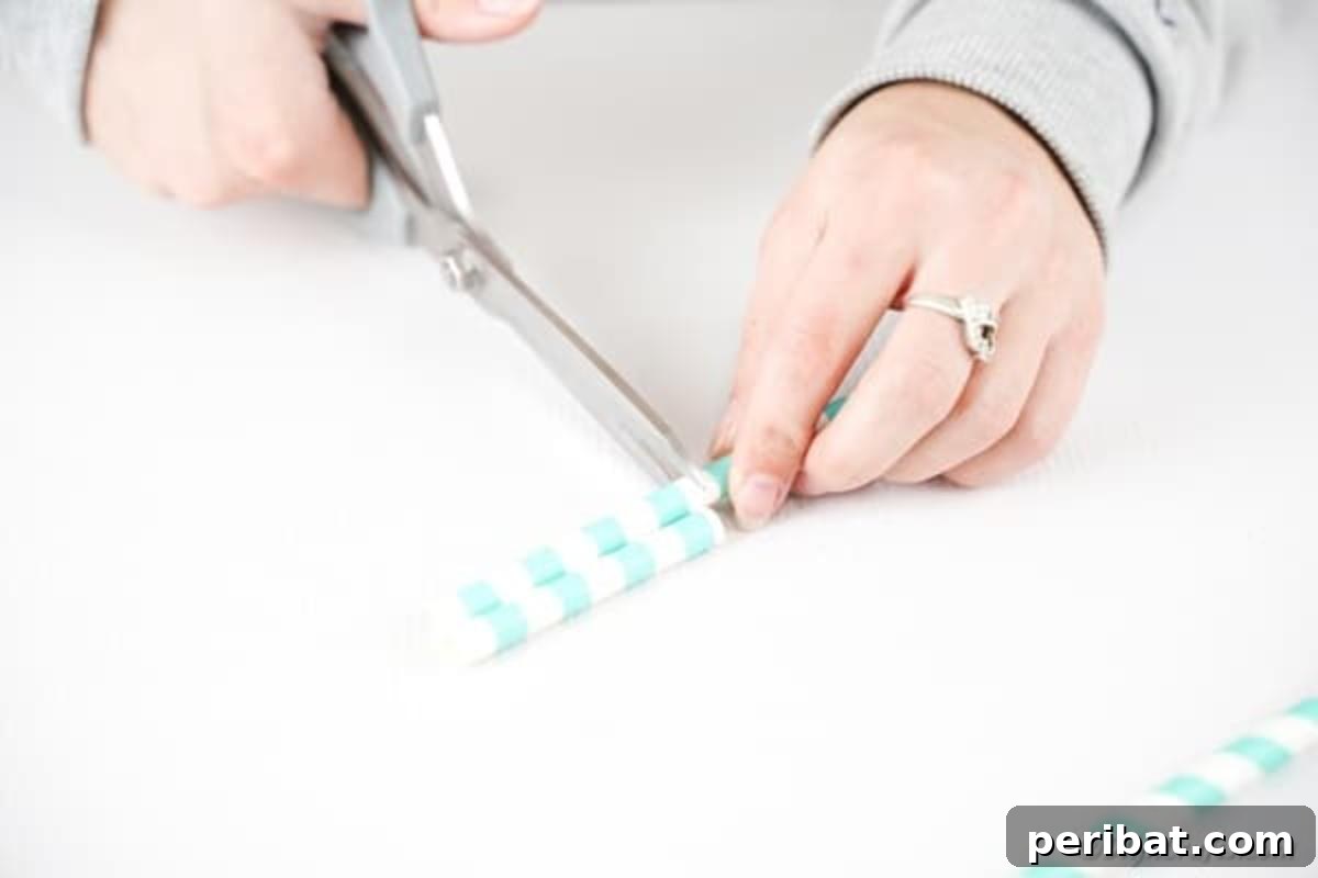 A pair of hands carefully cutting teal striped paper straws with scissors, preparing them for the crafting project.