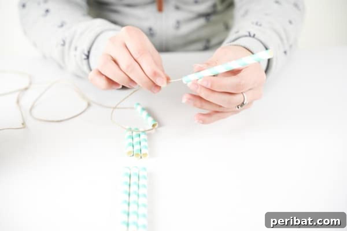Hands carefully threading twine through colorful paper straws, demonstrating the initial stage of assembling the planter.