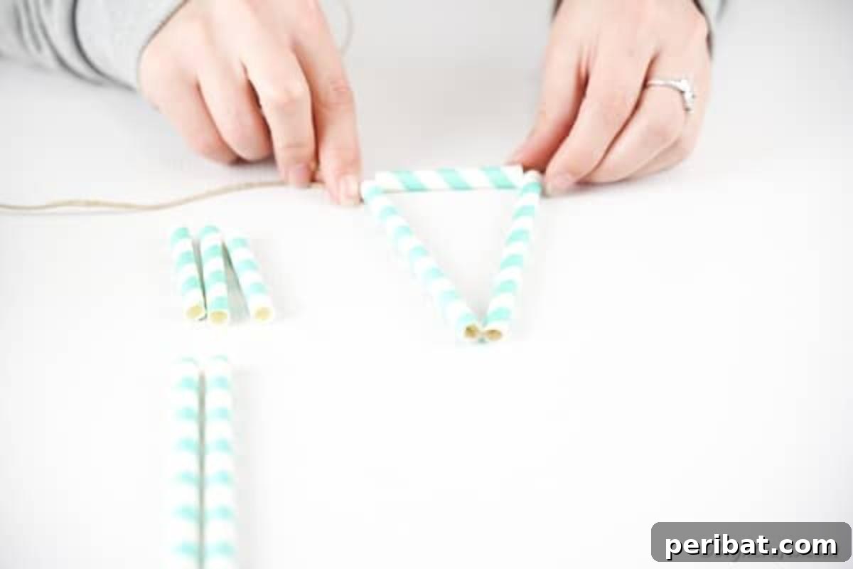 Close-up of hands adding paper straws to a piece of twine, bending the last straw to begin forming a triangular shape.