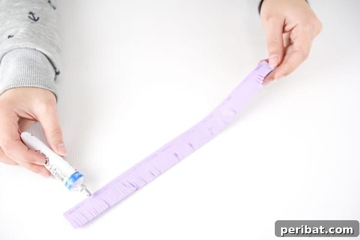 Applying a thin line of glue along the uncut edge of a fringed paper strip