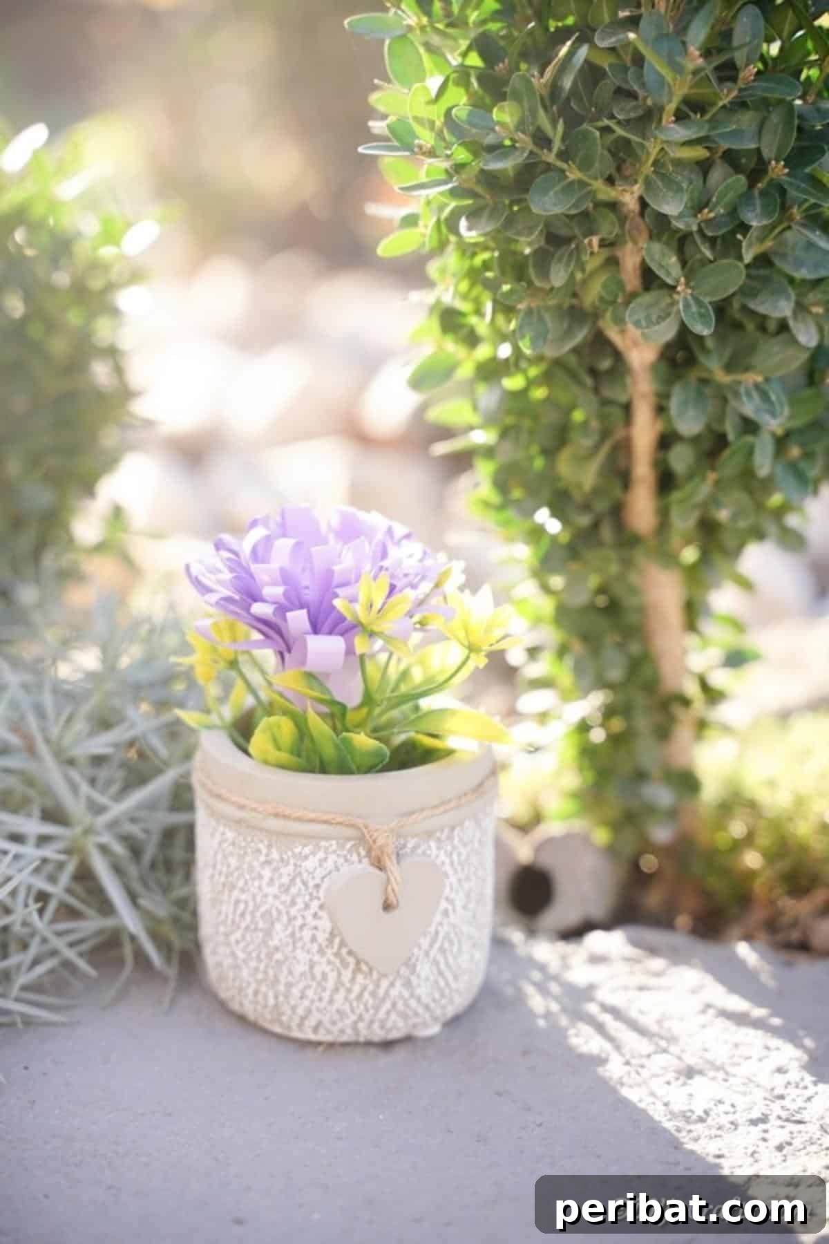 A single paper flower gracefully placed in a vase, sitting on a sidewalk in front of a green shrub