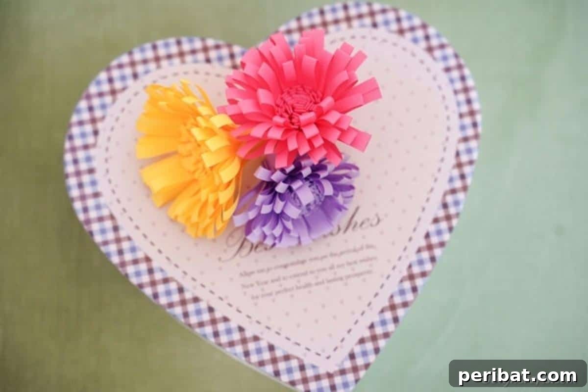 Close-up of pink, yellow, and purple paper flowers adorning the lid of a heart-shaped gift box