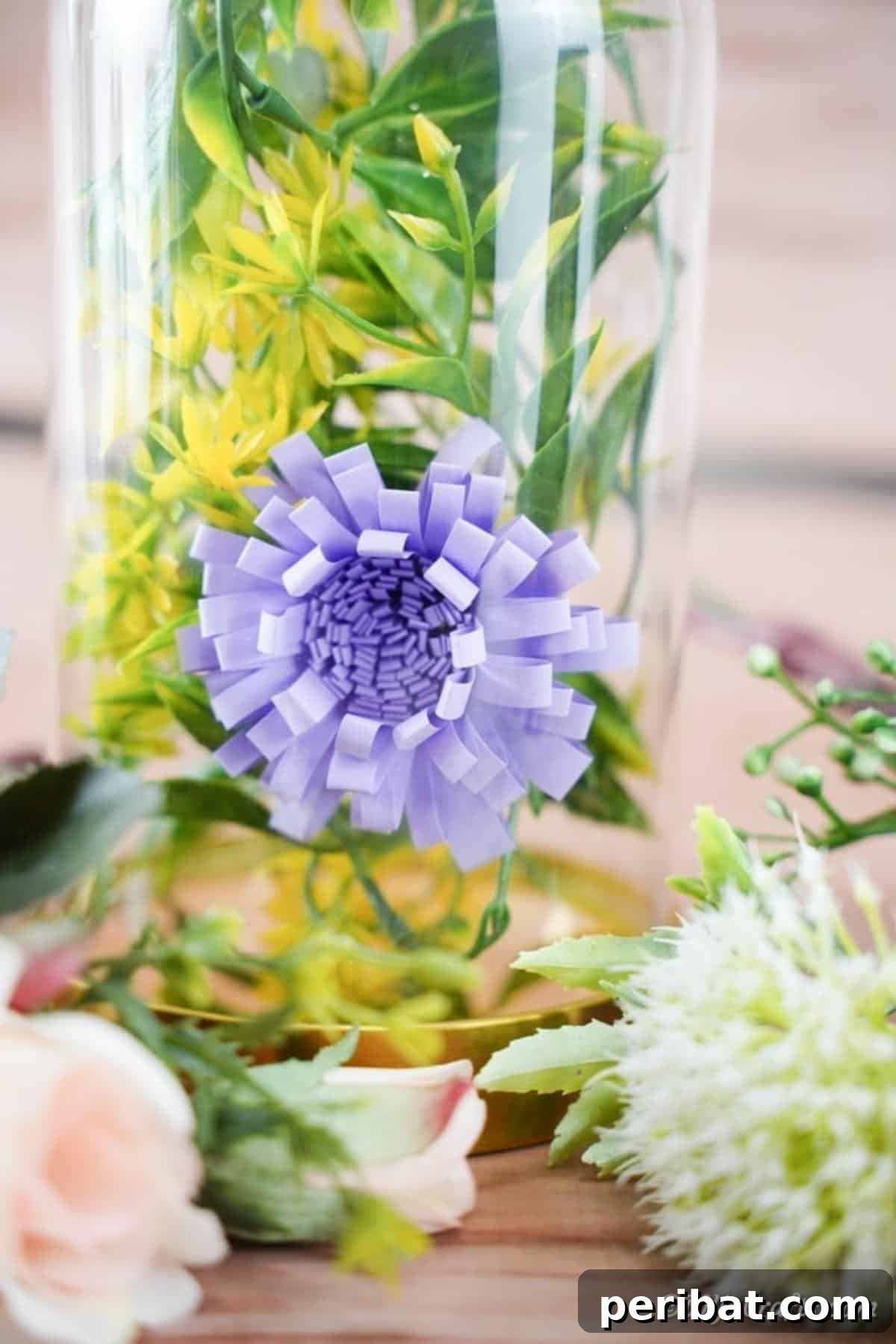 A single purple paper flower arranged elegantly inside a clear glass jar with lush green foliage