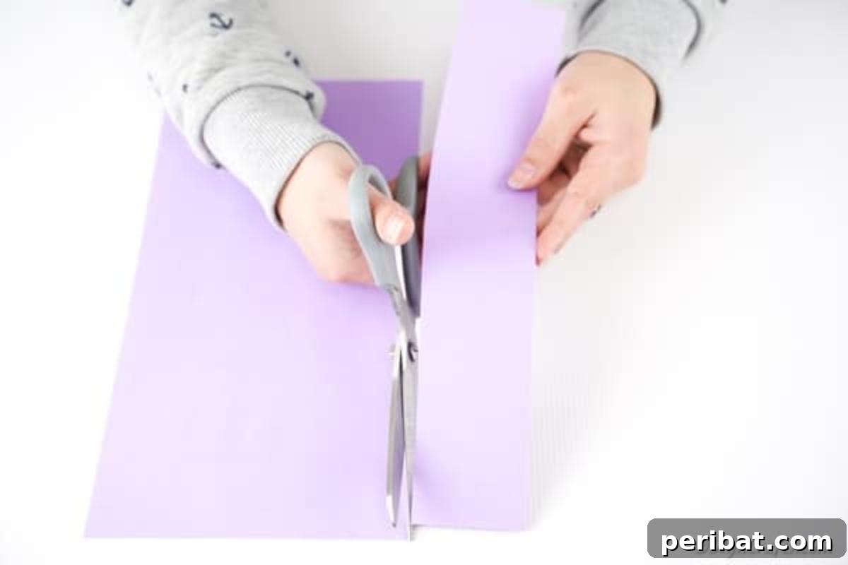 A hand cutting a narrow strip of paper vertically from a larger sheet