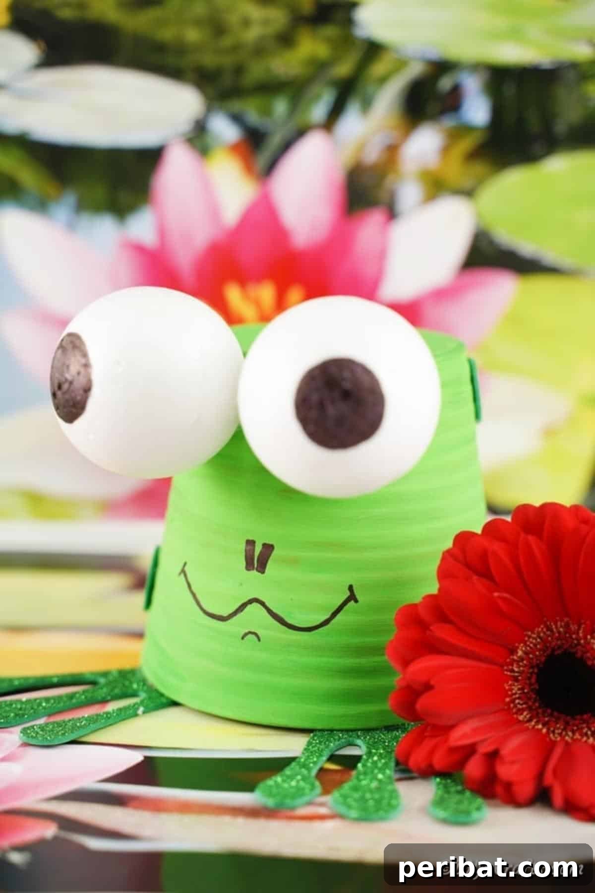 Whimsical Upcycled Flowerpot Frog Garden Art 4 A vibrant flower pot garden frog, painted green and decorated with foam details, sits on a textured surface with artificial red and pink flowers, making a cheerful outdoor statement.
