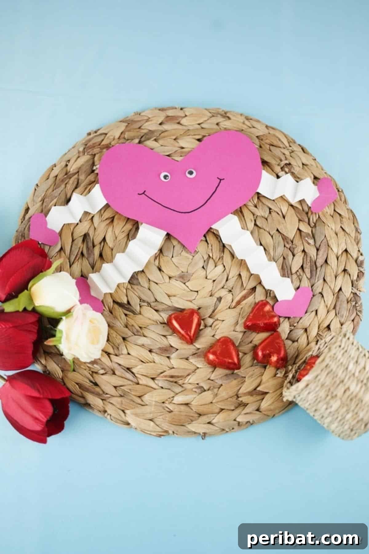 Little Hands, Loving Hearts: Kids' Valentine Paper Craft 16 A finished pink paper heart decoration resting on a woven mat against a blue background