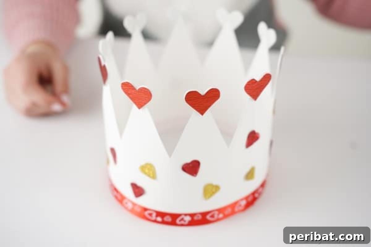 Easy Valentine Paper Crown Craft for Children 13 Hands meticulously add more heart decorations around the exterior of the paper crown, customizing its appearance.