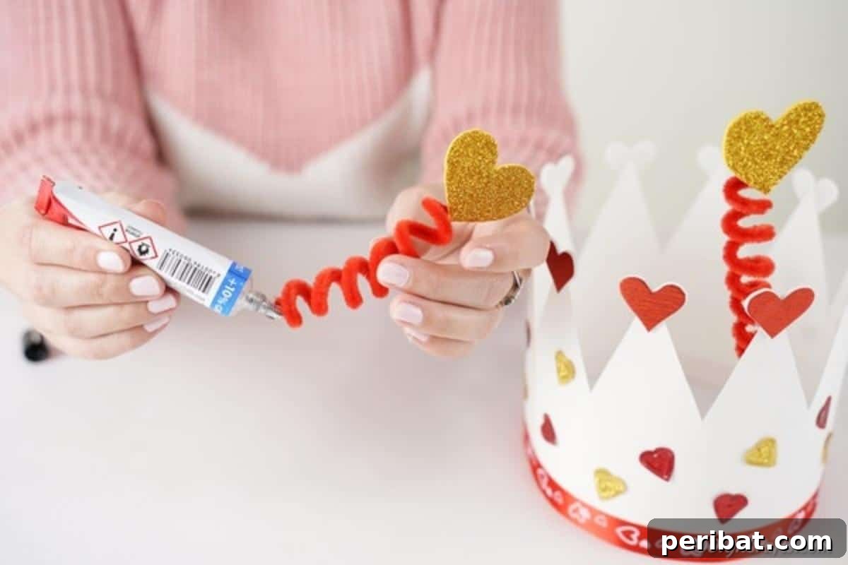Easy Valentine Paper Crown Craft for Children 15 A hand glues the spiral pipe cleaner toppers, adorned with hearts, to the inside of the paper crown, securing them in place.