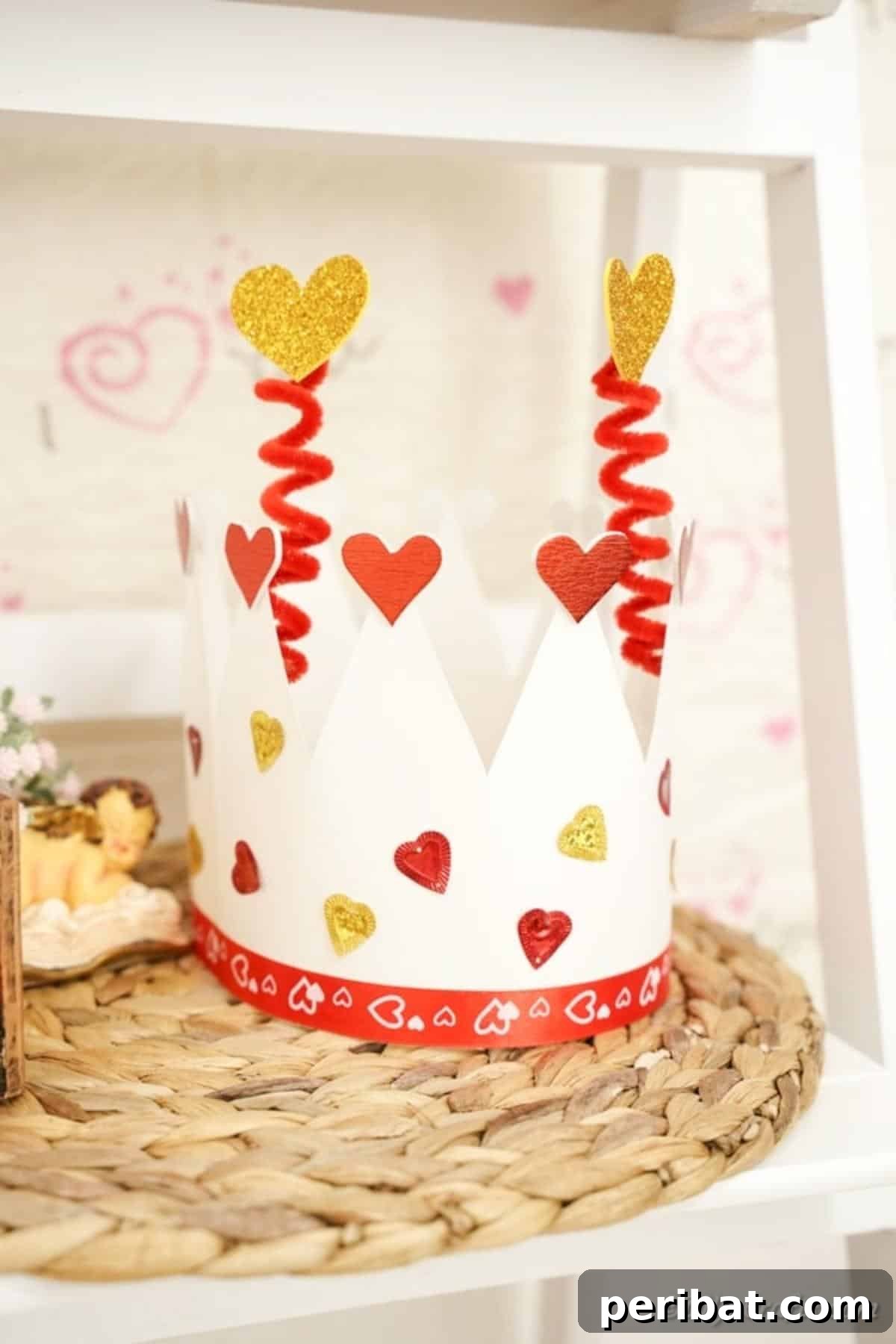Easy Valentine Paper Crown Craft for Children 5 A decorative Valentine's Day paper crown, featuring hearts and glitter, resting on a rustic woven mat.
