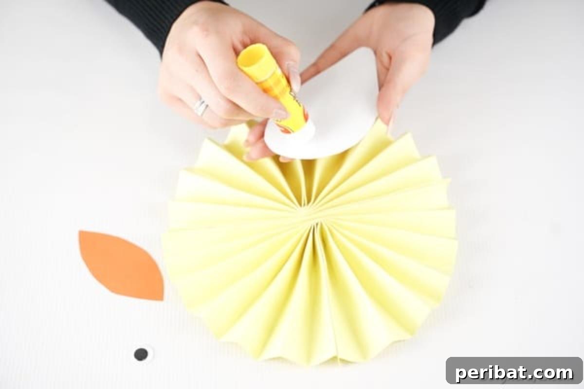 Simple & Sweet: Crafting Paper Birds with Kids 13 A hand gluing the patterned paper wing onto the center of the fanned yellow paper circle, carefully positioning it to form the body of the bird.