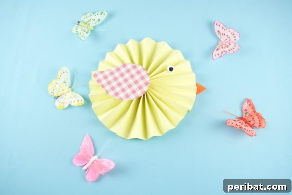 Simple & Sweet: Crafting Paper Birds with Kids 15 A cheerful yellow paper chick with a patterned wing, googly eye, and orange beak, beautifully displayed on a blue surface surrounded by delicate paper butterflies, creating a serene and playful springtime vignette.