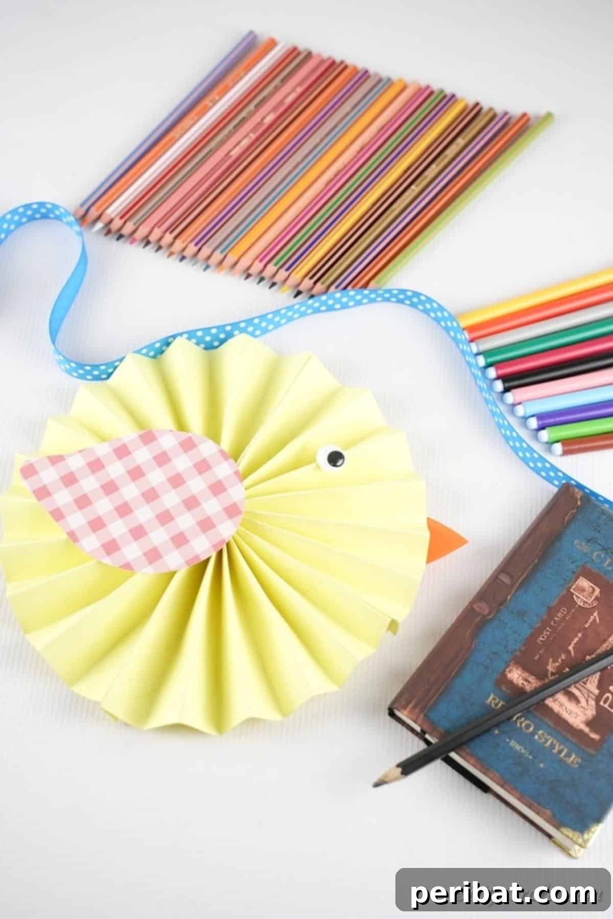 Simple & Sweet: Crafting Paper Birds with Kids 3 A charming finished paper bird laying on a wooden table, surrounded by colorful craft supplies like paper strips, a glue stick, and scissors, suggesting a creative workspace.