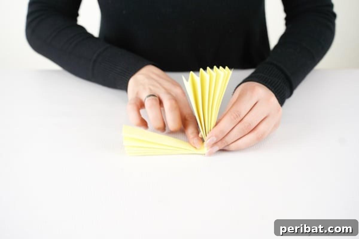 Simple & Sweet: Crafting Paper Birds with Kids 8 The previously accordion-folded yellow paper is now folded in half horizontally, forming a compact, fan-like semi-circle, ready for gluing to create the bird's body.