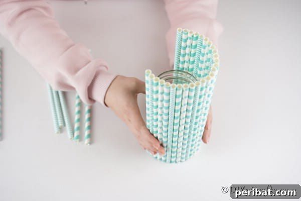 Continuing to glue straws onto the mason jar vase, creating a pattern