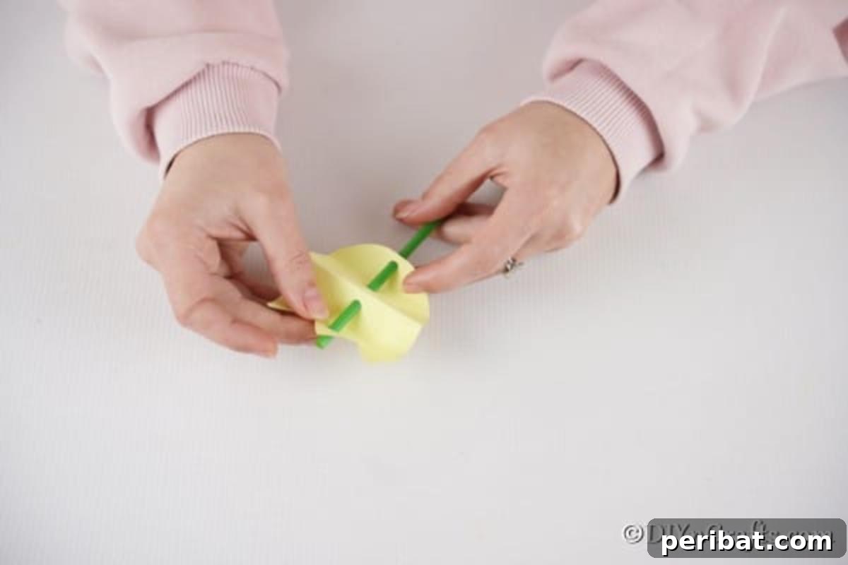 Create Charming Spring Paper Tulips 11 Sliding a green straw through the punched holes in the unfolded paper tulip to create the stem