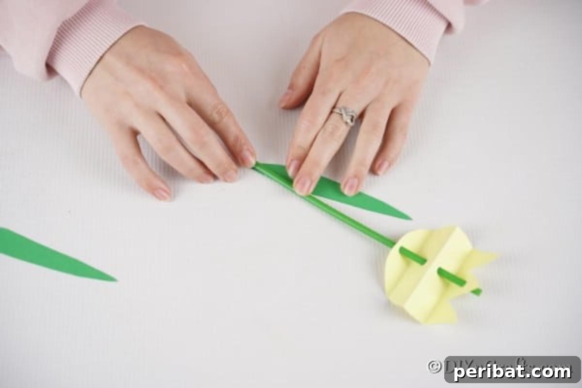 Create Charming Spring Paper Tulips 13 Attaching green paper leaves to the base of the straw stem of a paper tulip using glue