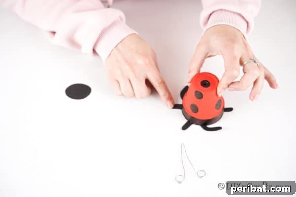 Adorable Upcycled Ladybug Planter Craft 13 The cut-out black paper legs are being glued onto the black rim of the flower pot.