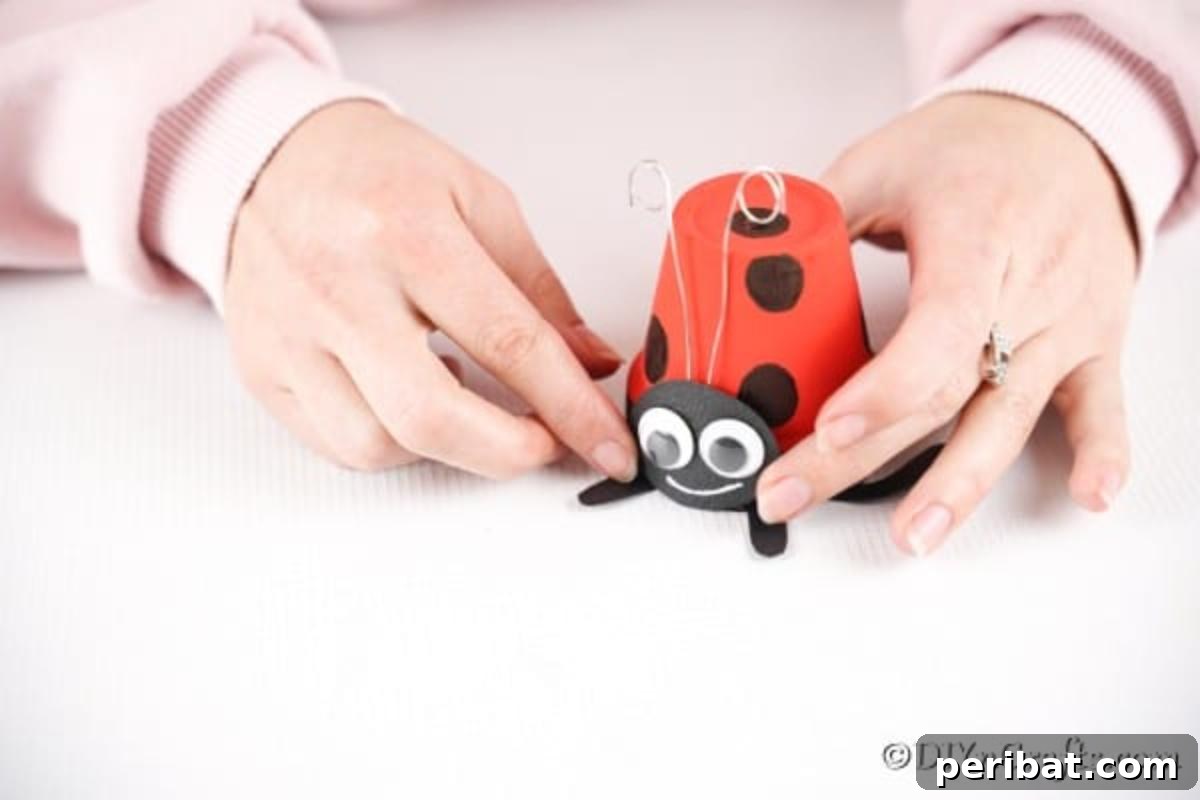 Adorable Upcycled Ladybug Planter Craft 15 The black oval face and wire antennae are being carefully glued onto the ladybug flower pot.
