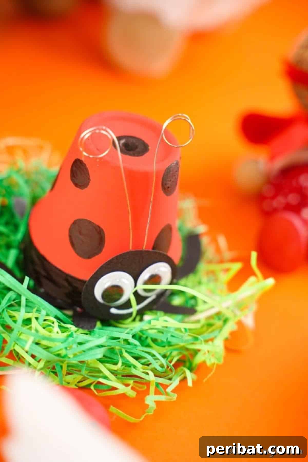 Adorable Upcycled Ladybug Planter Craft 5 A close-up of a finished ladybug flower pot sitting on vibrant green grass against an orange surface.