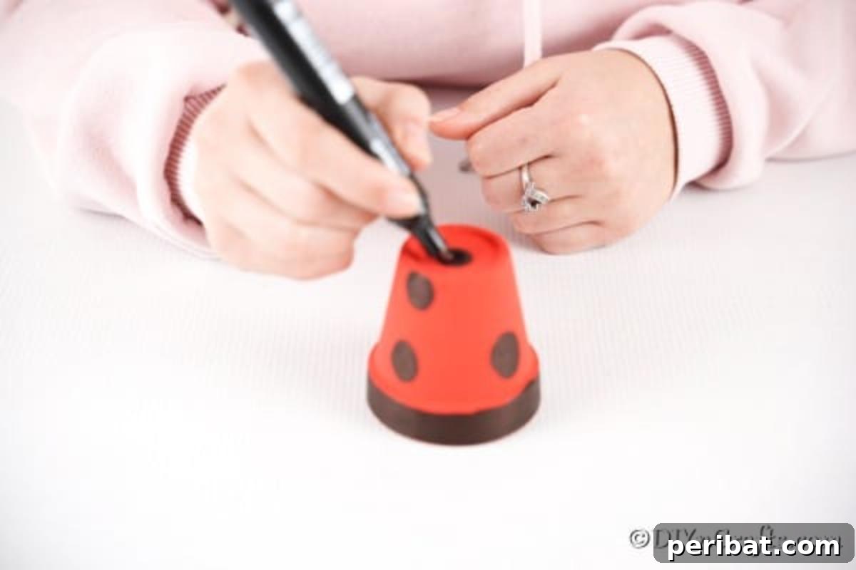 Adorable Upcycled Ladybug Planter Craft 10 Black dots are being drawn onto the red flower pot, forming the signature patterns of a ladybug.