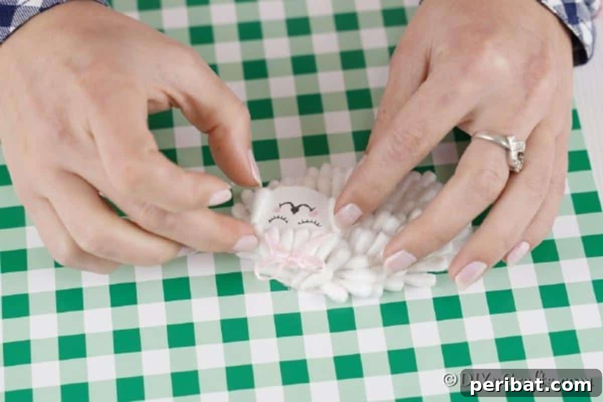 Gluing the finished face onto the fluffy cotton swab body and attaching a delicate pink ribbon bow to complete the lamb's look.