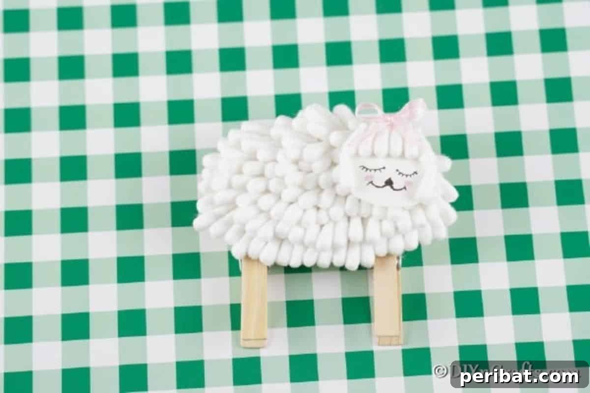 Finished cotton swab lamb sitting on green checkered paper, a charming handmade decoration for spring or Easter.